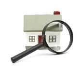 8539405-magnifying-glass-examining-model-home-isolated-on-white